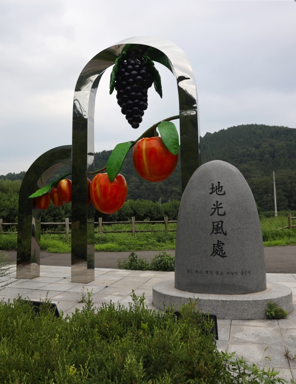 마을 입구에 세워진 마을의 대표 농산물 복숭아, 포도 모양의 조형물과 지광풍처(地光風處) 비석